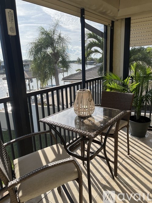 A table with chairs and a vase on a balcony overlooking a body of water.