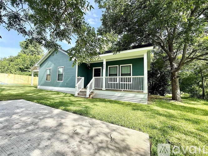 A green house with a porch and a driveway in front.
