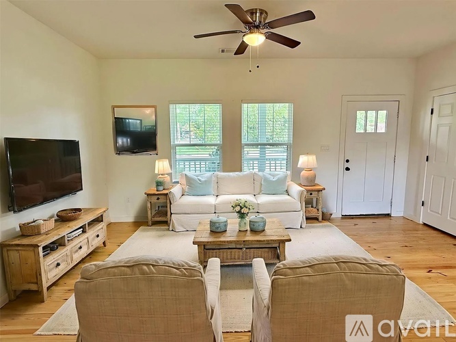 A living room with a white couch, a wooden coffee table, and a flat-screen TV mounted on the wall.