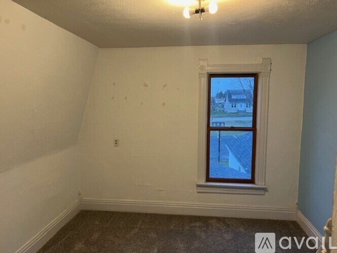 A room with a window showing a view of a house and a blue sky.