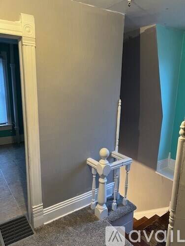 A white stair railing with a round finial is in the foreground of a room with a grey wall and a black door.