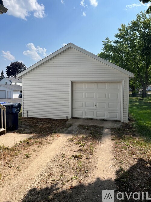 A small white garage with a closed door is situated in a yard.