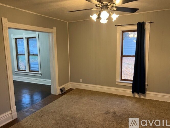 A room with a ceiling fan and two windows.