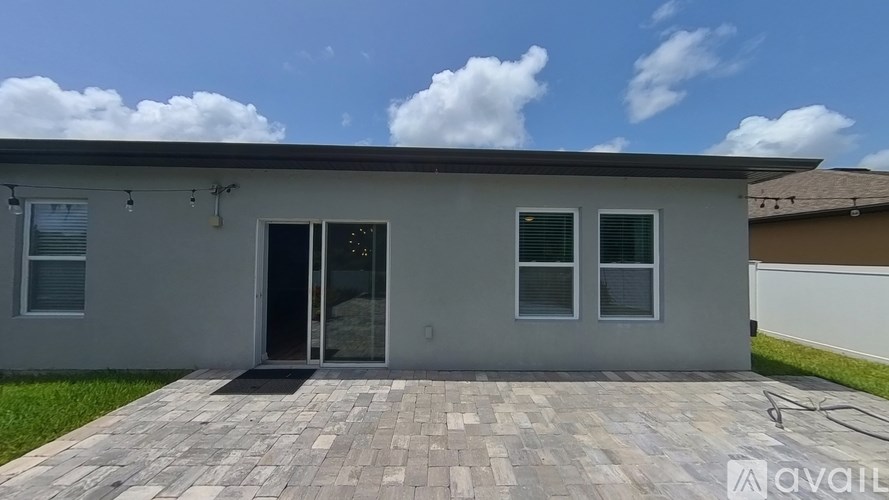 A house with a grey facade and a brick patio is available for rent.