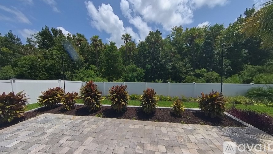 A garden with a circular brick patterned walkway and a white fence.