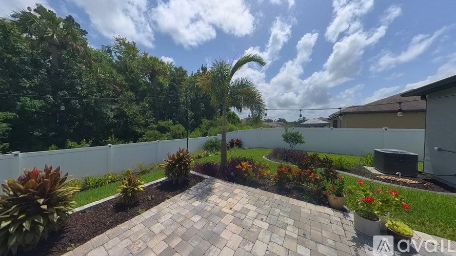 A backyard with a circular brick patio and a white fence.