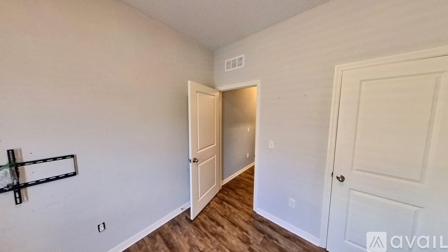 A room with a white door and a white wall with a black shelf on the left.