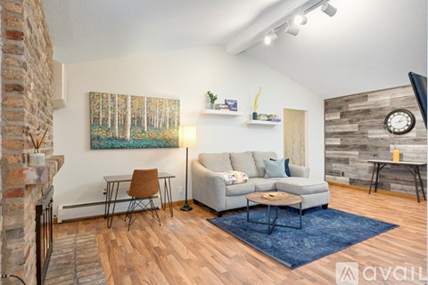 A living room with a grey couch, a brown chair, a blue rug, and a painting on the wall.