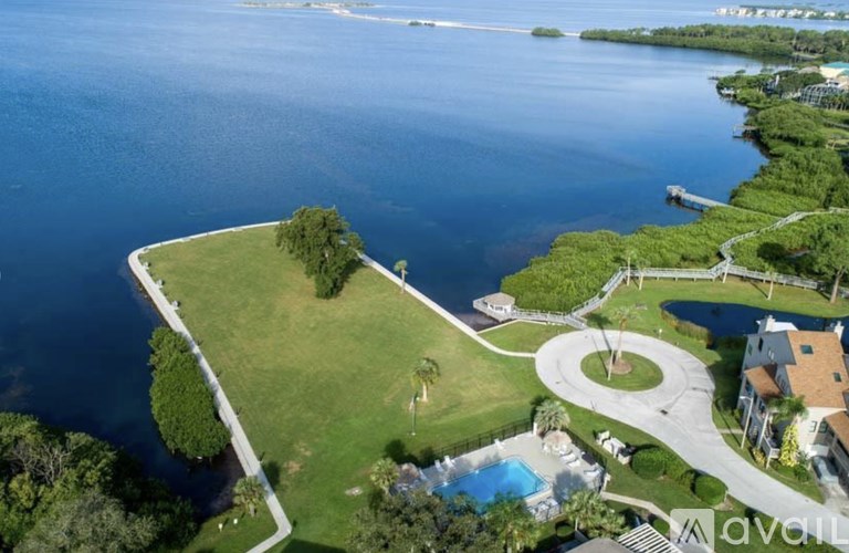 A large grassy area with a pool and a house is surrounded by water.