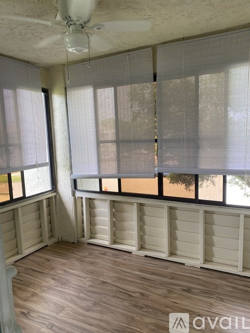 A room with a ceiling fan and large windows covered with blinds.