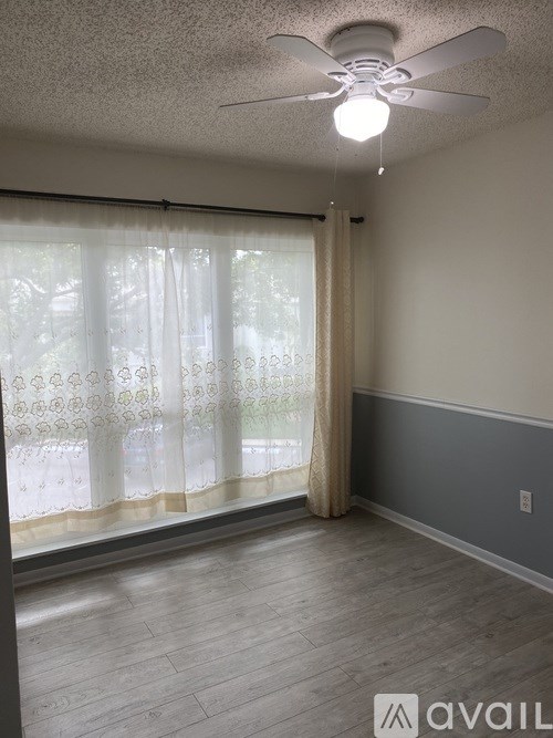 A room with a ceiling fan and a window with curtains.