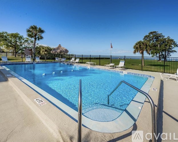 A large outdoor swimming pool surrounded by a fence and palm trees.