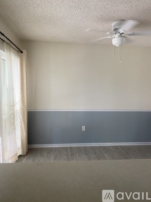 A room with a ceiling fan and a window with curtains.