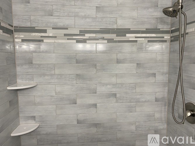 A shower area with a grey tile wall and a silver shower head.