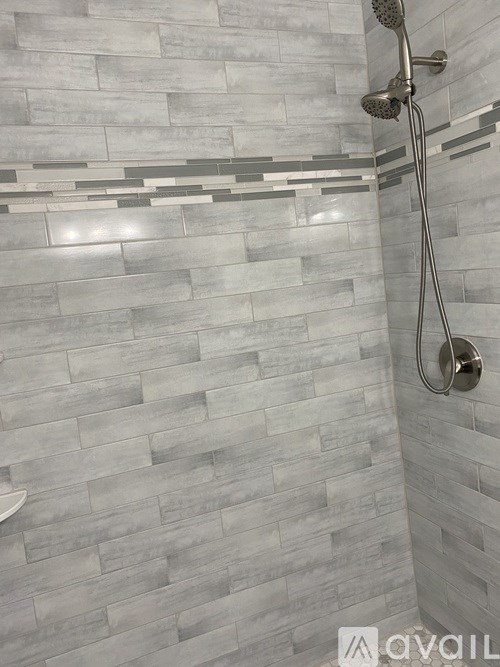 A shower with a silver shower head and a silver faucet.