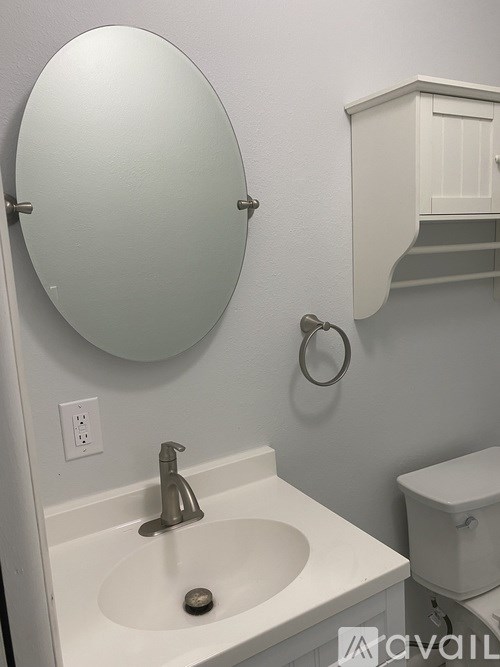 A white sink with a silver faucet and a round mirror above it.