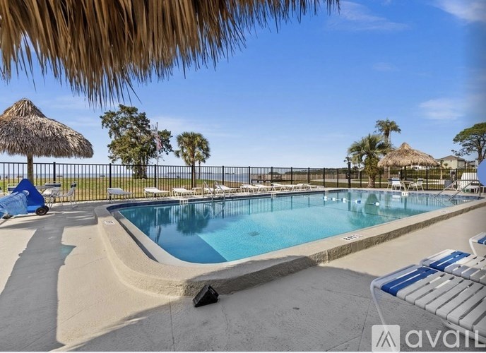 A large outdoor swimming pool surrounded by a fence and palm trees.