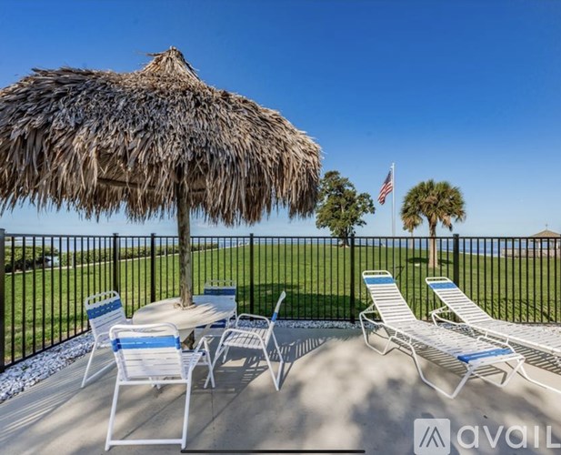 A patio with a thatched umbrella and chairs overlooking a pool.