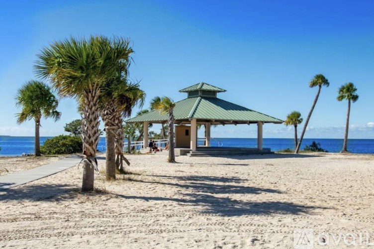 A gazebo sits on a beach with palm trees and the ocean in the background.