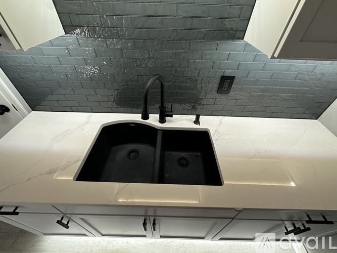 A kitchen with a sink and a grey tiled wall.