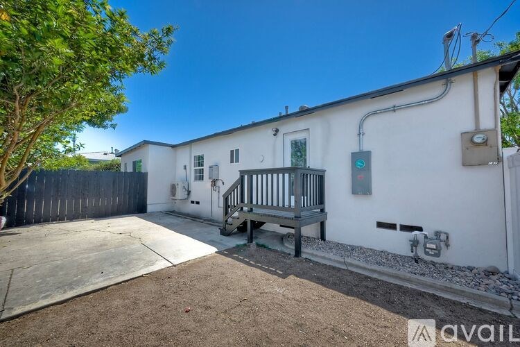 A white house with a tree in front and a wooden deck.