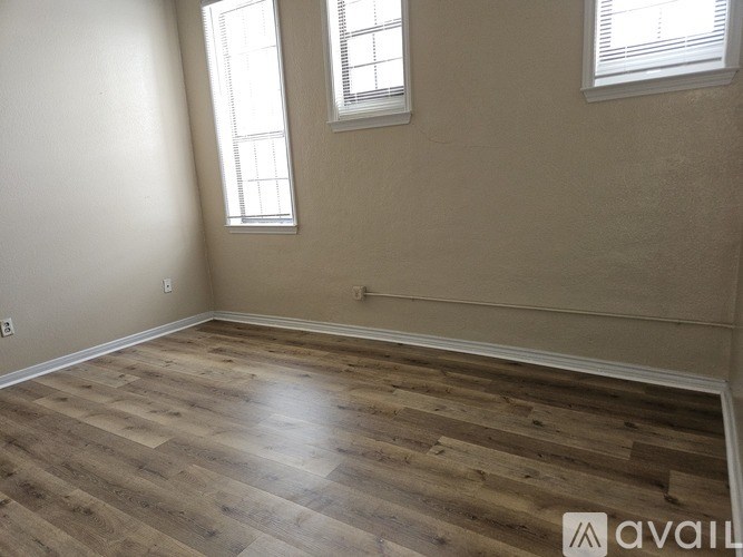A room with wooden flooring and two windows.