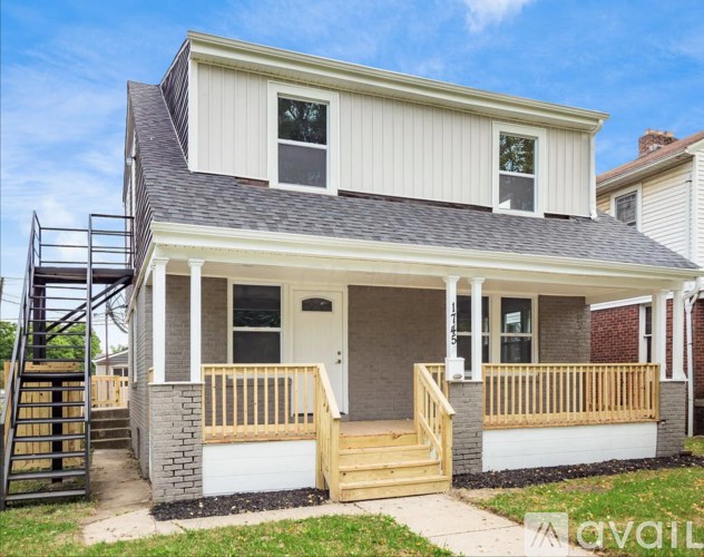 A house with a white exterior and a grey roof with a balcony and a staircase.
