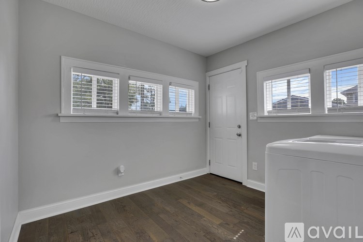A room with wooden floors and white walls, featuring a white door and two windows with blinds.