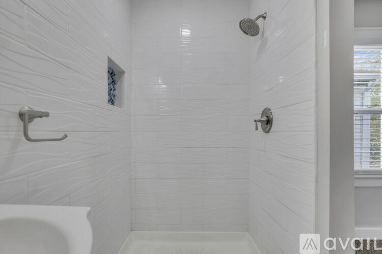 A white tiled bathroom with a shower and a window.