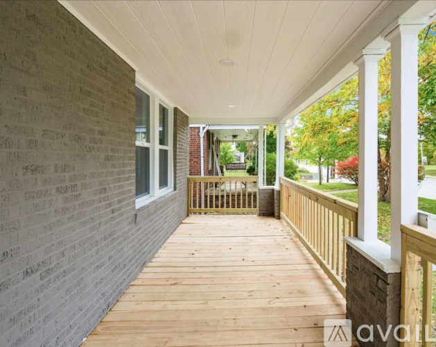 A wooden porch with a white ceiling and brick wall.
