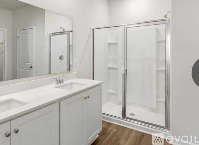 A white bathroom with a double sink and a walk-in shower.