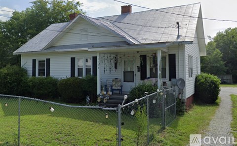 A white house with a grey roof and a fence in front.