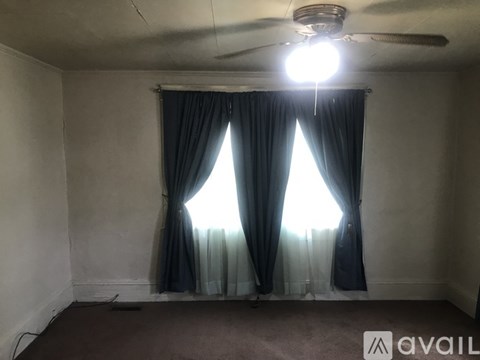 A room with a ceiling fan and a window with curtains.