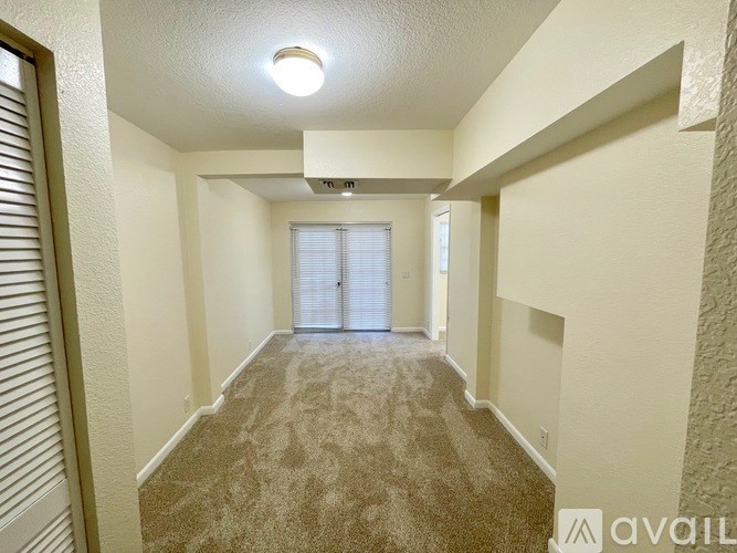 A long hallway with a carpeted floor and a window with blinds.