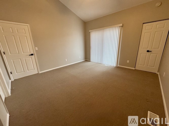 A room with carpeted floor, two doors, and a window with blinds.