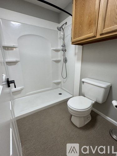 A white toilet sits in a bathroom with a white tub and wooden cabinets.