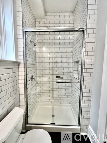 A white tiled shower with a glass door and a white toilet.