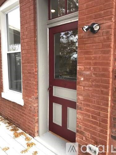 A red door with a black handle and sidelights is on a brick building.