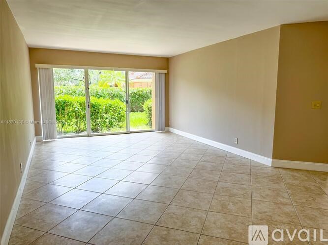 A spacious room with tiled flooring and sliding glass doors leading to a garden.