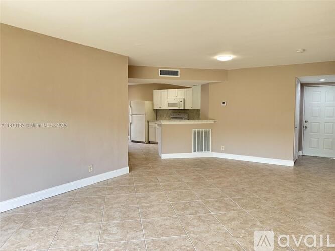 A spacious living room with beige walls and a kitchen area in the background.