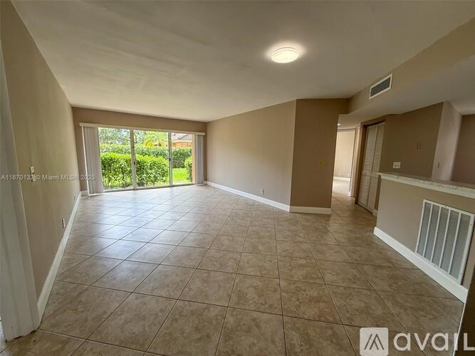 A spacious room with tiled flooring and a sliding glass door leading to a garden.