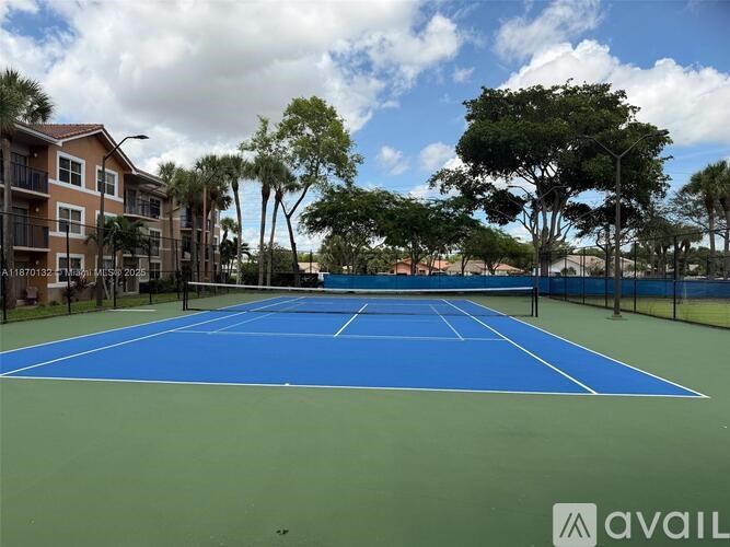 A tennis court is surrounded by trees and apartment buildings.
