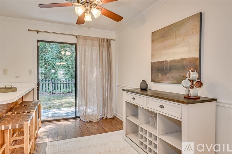 A room with a ceiling fan, a painting on the wall, and a wooden table with a vase on it.