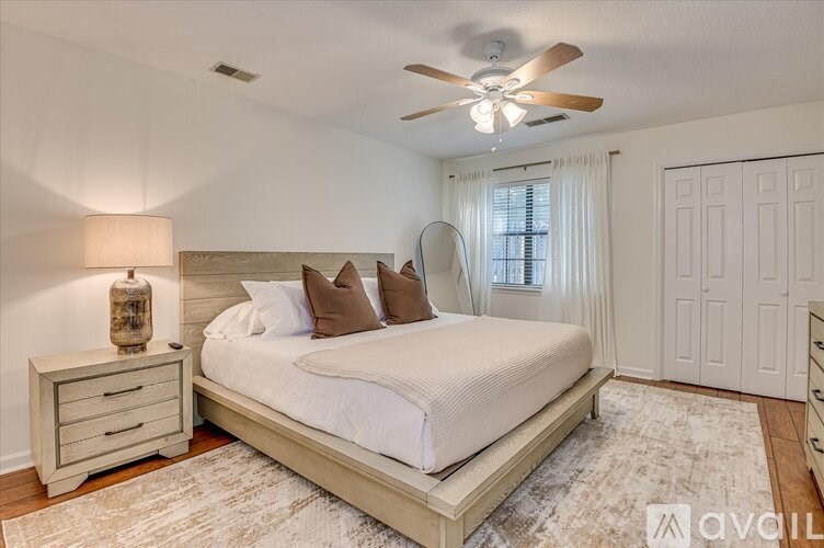 A bedroom with a large bed, a nightstand with a lamp, and a ceiling fan.
