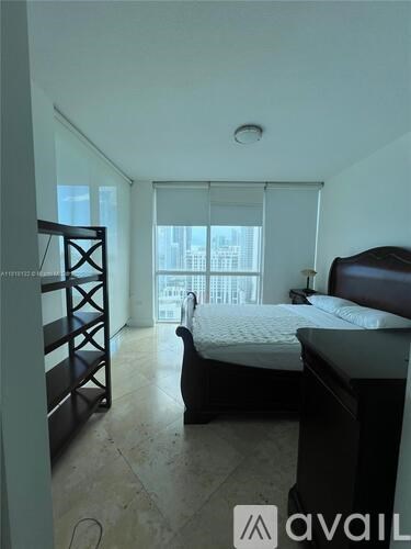 A bedroom with a bed, a chair, and a balcony with a view of the city.