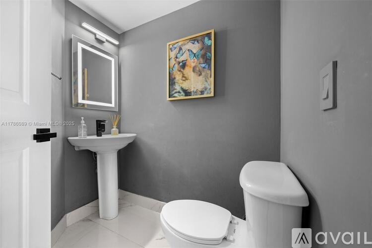 A bathroom with a white pedestal sink, toilet, and a painting on the wall.