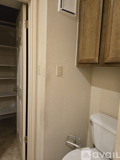 A white toilet is in a small bathroom with a white door and a white light switch.