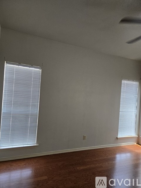 A room with wooden floors and two windows with blinds.