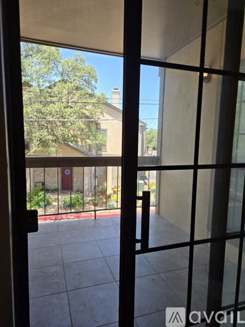 A view from inside a room looking out through a glass door to a patio with a tree and a building in the background.