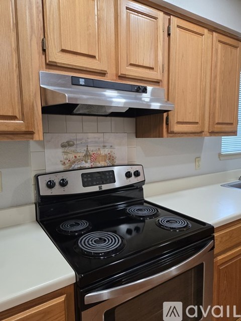 A black stove top oven with four burners and a digital display is installed in a kitchen with wooden cabinets.